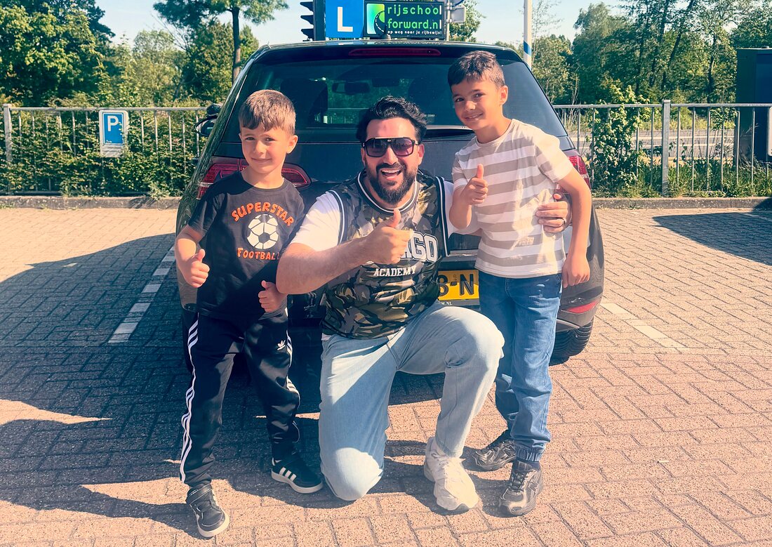 Alaa Eddine hurkt lachend met twee jonge supporters bij de zwarte lesauto van Rijschool Forward