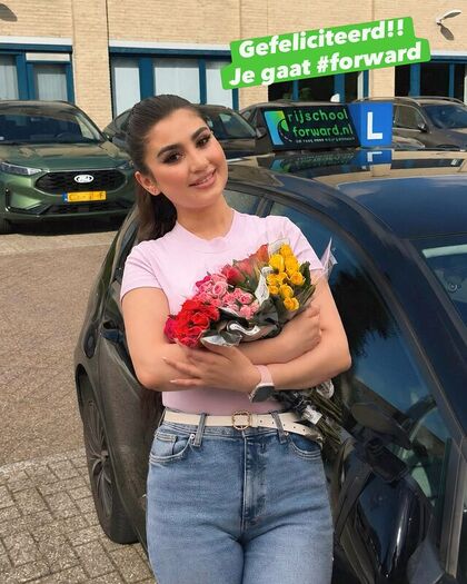 Geslaagde leerling met een bos bloemen naast de lesauto