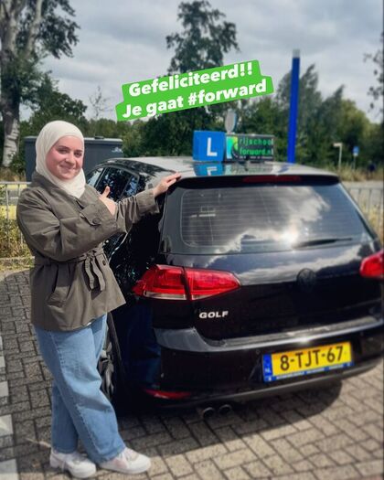 Geslaagde leerling naast de lesauto met het groene felicitatiebord