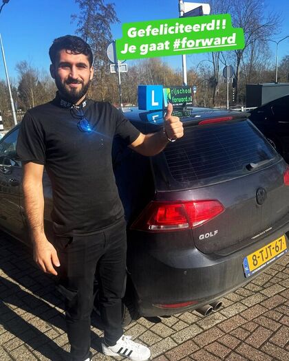 Geslaagde leerling met duim omhoog achter de lesauto
